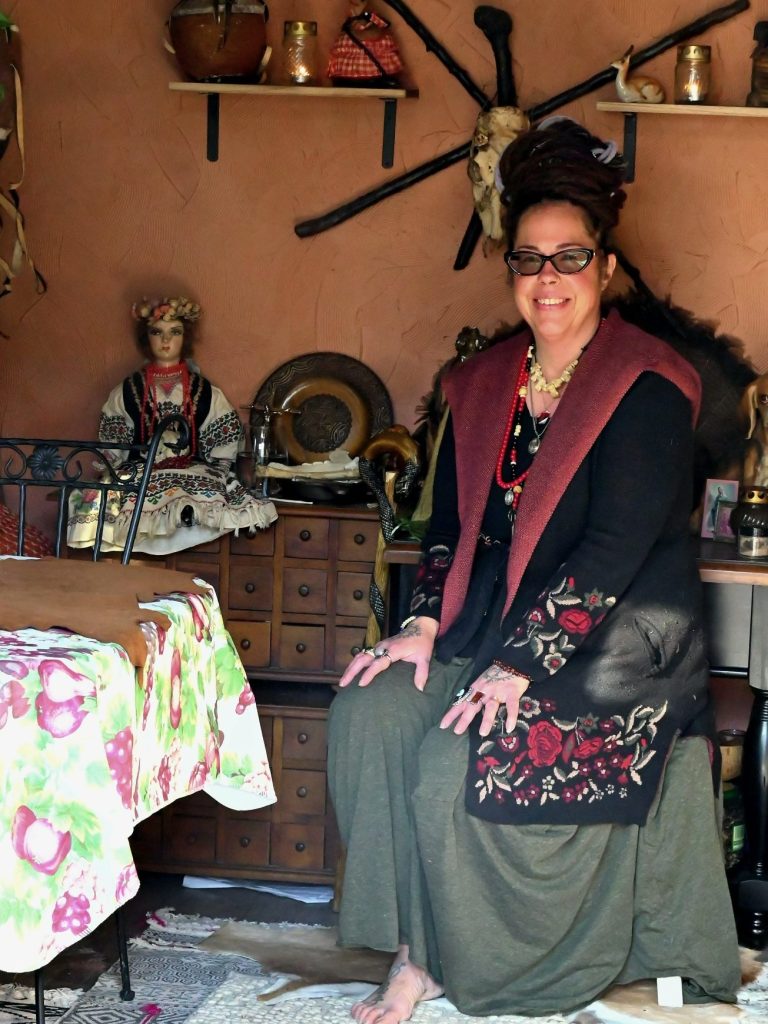 Woman sitting on a chair in a decorated room, wearing a long skirt and a colorful shawl.